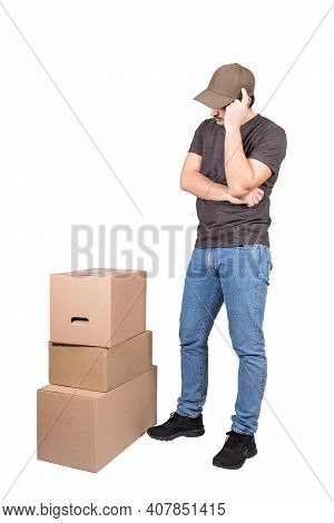 Thoughtful Delivery Man Wearing Cap, Full Length Portrait, Stands Near Cardboard Parcel Boxes, Isola