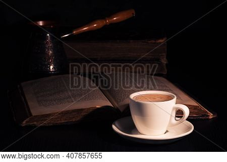 Cup Of Hot Coffee, Copper Cezve And Open Torah Page On Black Wood Table In The Dark. Closeup