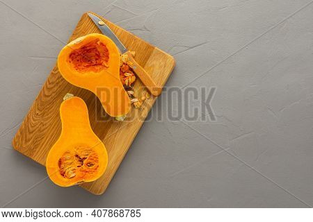 Raw Organic Butternut Pumpkin Or Gramma Cut In Half Close-up On Wooden Board With Knife On Gray Conc