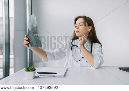 Young Caucasian Woman Doctor Wearing White Medical Coat And Stethoscope Holds The X-ray