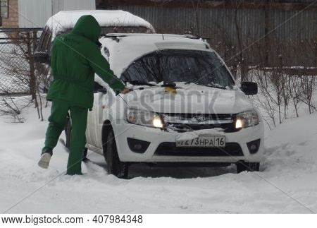 Kazakhstan, Ust-kamenogorsk, February 7, 2020: Man Cleaning Car From Snow In Winter. Green Clothes. 
