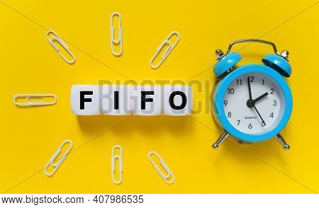 Finance And Economics Concept. On A Yellow Background, A Blue Alarm Clock, Paper Clips And White Cub