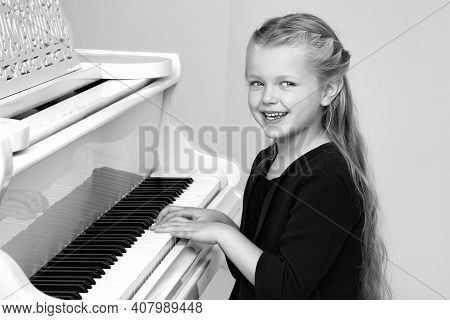 Beautiful Little Girl Playing On White Grand Piano. Black And White Shot Of Pretty Long Haired Girl 