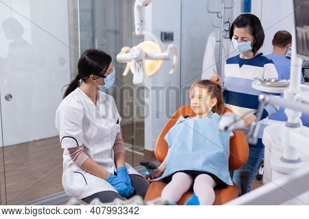 Dentist Wearing Face Mask In The Course Kid Examination With Dental Bib In Dentistiry Office. Dentis