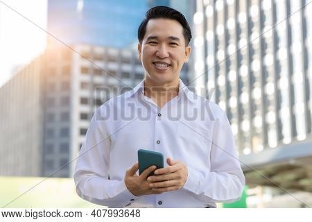 Portrait Happy Asian Man Holding Smart Phone And Looking At Camera With Smile Face In Cityscape Back