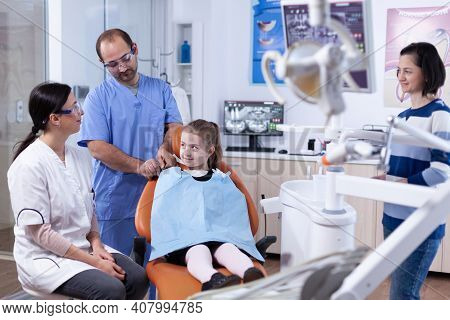 Little Girl Wearing Dental Bib Sitting On Chair In Dentist Office During Tooth Examining .child With