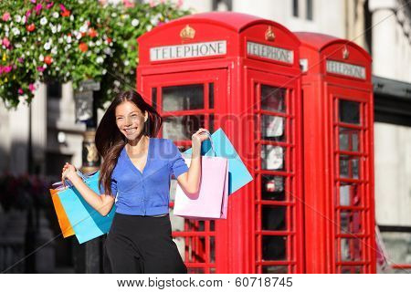 England London shopping woman shopper holding shopping bags by red phone booth. Female shopper smiling in London, England, United Kingdom during spring or summer. Mixed race Asian Caucasian model.
