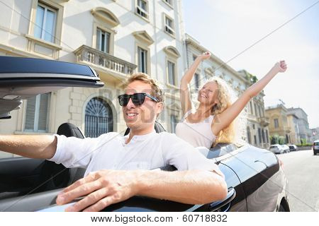 Car people - man driving with happy woman. Male driver wearing sunglasses. Young couple having fun in car driving on travel vacation together. Lifestyle with beautiful cheerful lovers.