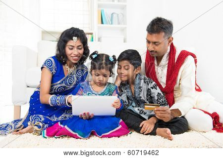 Indian Asian family using tablet pc computer online shopping with credit card at home. India family living lifestyle. Happy smiling parents and children.