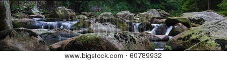 Wide small waterfalls, big pebbles, forest on background
