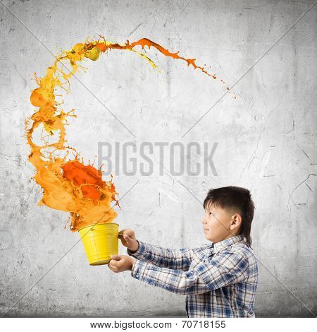 Young boy splashing colorful paint from bucket