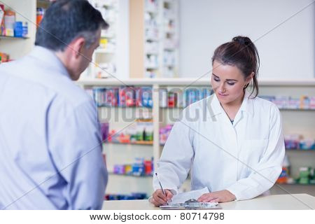 Trainee writing prescription in front of a customer in the pharmacy