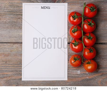 Menu sheet of paper with cherry tomatoes on rustic wooden surface background