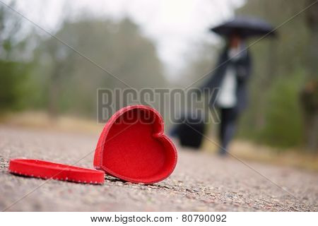 Red heart on the road and woman with luggage and umbrella