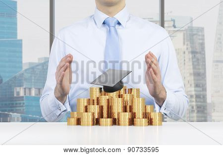 Student Is Placing His Hands Over The Graduation Hat And Coins Pyramid. A Concept Of A High Price Fo