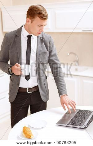 Businessman standing with cup of coffee using computer