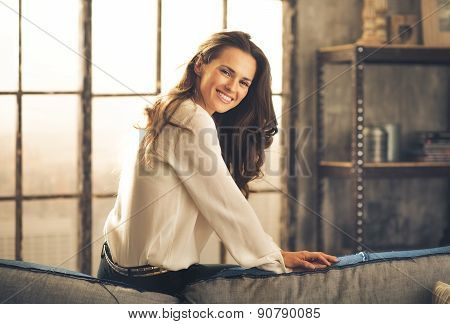 Elegant Woman Sitting On Back Of Sofa Smiling Over Shoulder