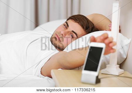 Beautiful young man waking up with mobile alarm clock
