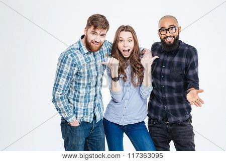 Beautiful amazed young woman standing and pointing on her two bearded handsome friends