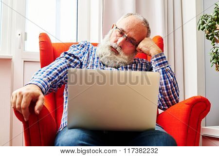 fatigued senior man sitting on the red chair and looking at laptop