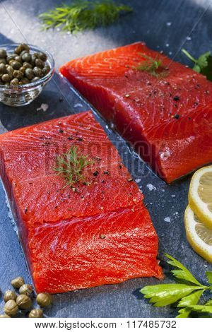 Two pieces of raw wild salmon fish steaks with lemon, capers and herbs, ready to cook