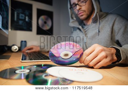 Confused thoughtful young software developer in hoodie and glasses working at home and choosing CD with database