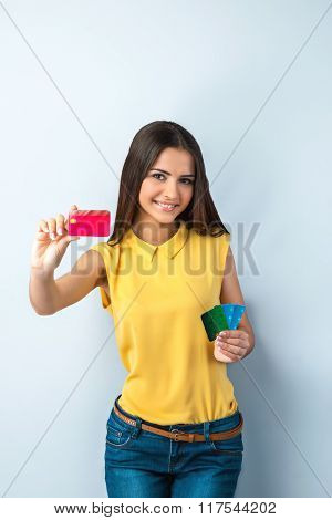 Photo of beautiful young business woman standing near gray background. Woman with yellow shirt looking at camera, smiling and showing credit cards