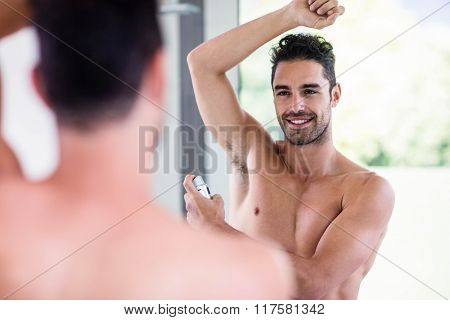 Handsome shirtless man putting deodorant in the bathroom