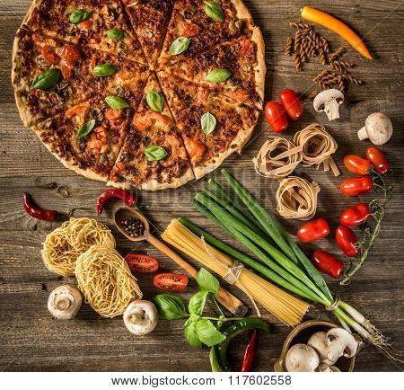 Italian food background with pizza, raw pasta and vegetables on wooden table
