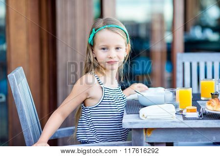 Adorable little girl having breakfast at outdoor cafe