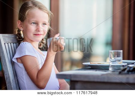 Adorable little girl having breakfast with tea at outdoor cafe