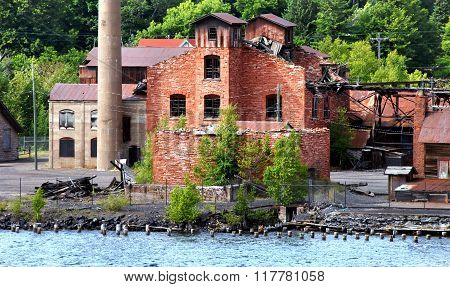 Historic Quincy Copper Smelter lays abandoned and empty. Buildings have fallen into ruin with rusting metal and broken windows. Smelter sits on the shore of the Portage Lake near Hancock Michigan.