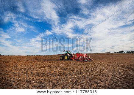 Farmer With Tractor Seeding Crops At Field