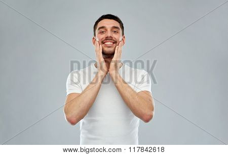beauty, skin care, grooming and people concept - happy young man touching his face applying aftershave over gray background