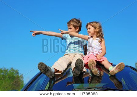 Liten pojke och flicka sitter på biltaket på blå himmel, titta till vänster sida och genom Finger
