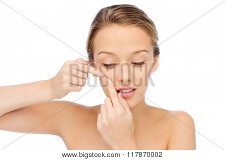 beauty, people, skincare and health concept - young woman squeezing pimple on her face