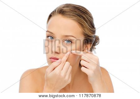 beauty, people, skincare and health concept - young woman squeezing pimple on her face