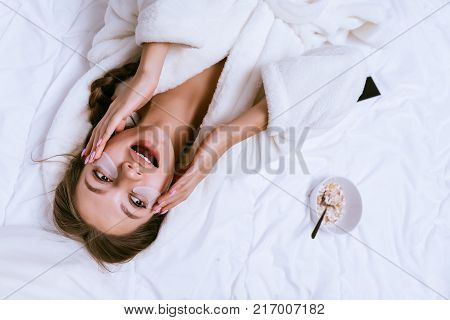 the girl woke up early, lying on a bed in a white coat, under her eyes silicone patches against blue circles