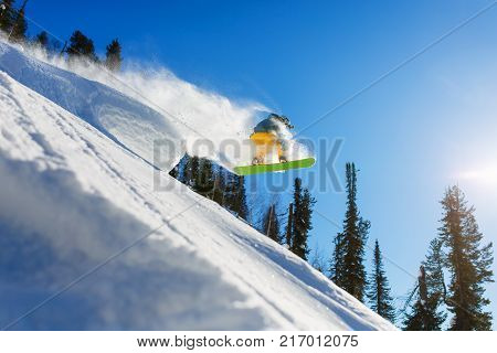A snowboarder jumps from a springboard in the high mountains on a sunny day. Sun rays white snow and clear weather blue sky.