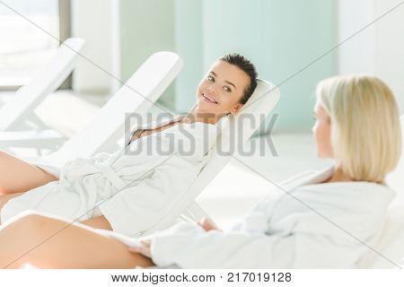 happy young women relxing on sunbeds at spa center