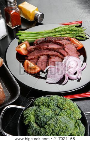 business lunch fresh roast beef meat slices on black plate wotj cutlery asparagus boiled broccoli rye bun on wooden table