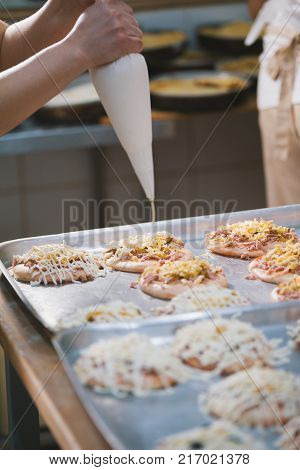 Cook puts the sauce on the mini pizza in the bakery close-up