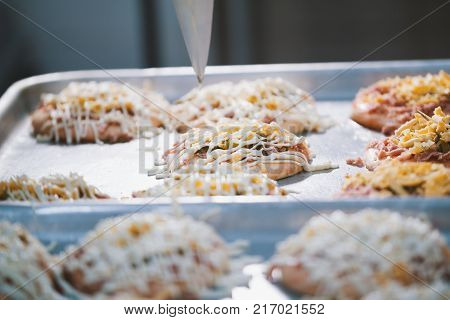 Cook puts the sauce on the mini pizza in the bakery close-up