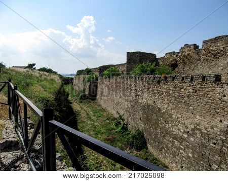 The moat near the stone wall of the Akkerman fortress in Bilhorod-Dnistrovskyi (Ukraine). A dilapidated ancient wall a trench overgrown with grass blue sky and sea away on the horizon