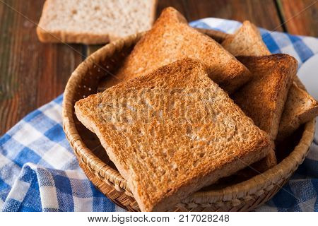 Breakfast background, white bread toasts in wicker breadbasket on checkered table napkin half covering wooden table, closeup