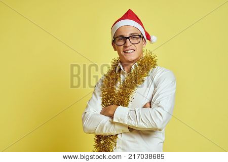 a man with tinsel on his neck, in a white shirt and glasses, his hands are folded on his chest, yellow background, free space for copying.