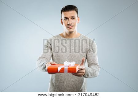 Take it. Attractive man wrinkling forehead and expressing positivity while holding red box