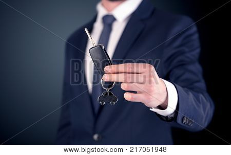 Young businessman hand over keys with empty dark background
