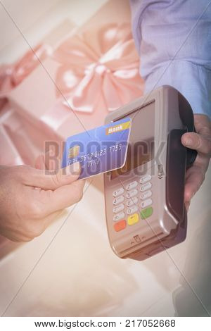 Hand holding contactless credit or debit card over wireless payment terminal at shop with gifts in the background 