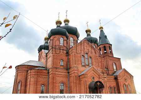 Church of a red brick with a black dome and a cross against the sky